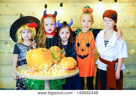 Happy group of witch children pirate and demons during Halloween party playing around the table with pumpkins