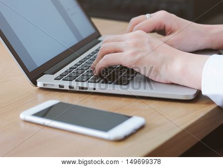 woman typing on laptop with smartphone on the table in office or home