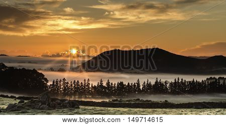 Orange red sunrise coming up over mountain and a foggy tree filled landscape