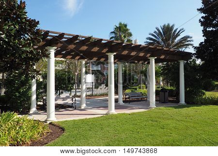 outdoor pavilion with a wood roof and columns. There are benches under the pavilion and it is surrounded by lush vegitation