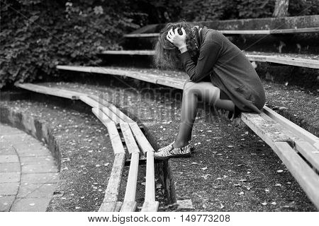 Ginger woman sitting on the bench in the park head in the hands despair pose black and white