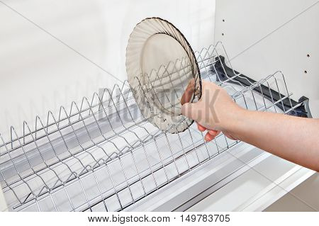 Close-up housewives hand takes a plate from the wall kitchen cabinet with wire dish drainer inside.