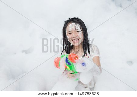 Little asian girl smiling and holding squirt gun in foam party