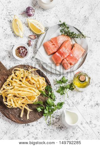 Ingredients for cooking lunch - raw salmon dry pasta tagliatelle cream olive oil spices and herbs. On a light background top view