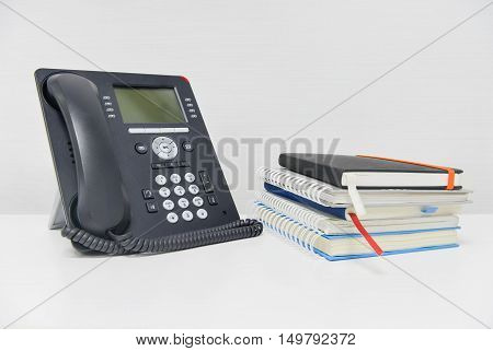 Black IP Phone and stack of books on the white table
