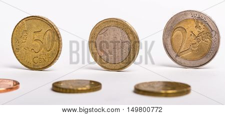 Different Euro coins standing upright and laying flat against a white background.