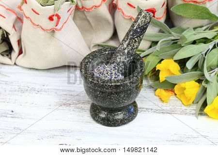 Mortar with lavender fresh sage herb and evening primrose flower and dried medicinal and culinary herbs in bags