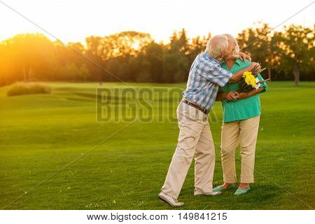 Elderly couple is kissing. Man and woman with flowers. Happy anniversary, darling. You're the best.