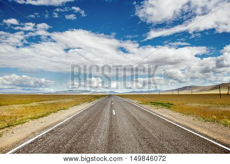 Straight road goes to horizon on background of sky and mountains. Altay mountains, Siberia, Russia.