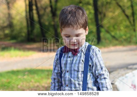 Smiling little boy with bow tie looks down in sunny green park