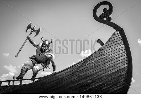 Strong angry bearded Viking with axe jumping from his ship to attack and war. black and white.
