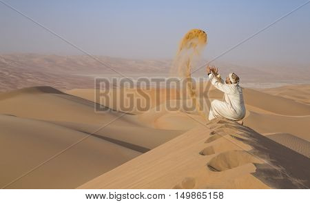Man in traditional outfit in a desert at sunrise throwing sand