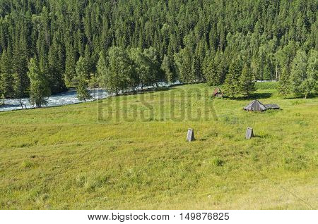 Abandoned cattle-ranch on the banks of river Kucherla. Altai Mountains Russia. Sunny summer day.