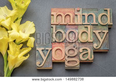 mind, body, yoga word abstract - text in letterpress wood type printing blocks against slate stone with yellow gladiola flower