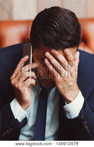 Depressed businessman talking on phone. Man holding palm on face being shocked of information. Failure, bankruptcy concept. Unsuccessful negotiations.