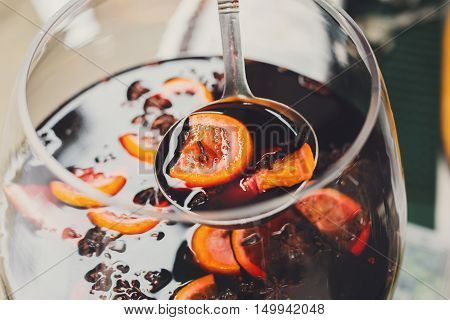 Making hot alcohol, mulled wine for sale at country fair. Glintwine from red wine with citrus and cloves in big glass, mixed with soup ladle. Closeup