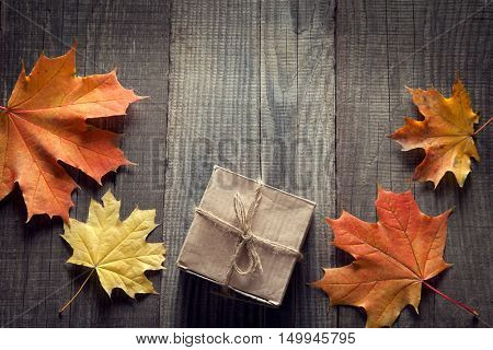 cardboard box tied with string on a bow on a wooden background in autumn leaves, holiday gift on Thanksgiving Hellouin. view from the top. copy space