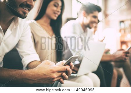 Technologies making life easier. Group of young people using different gadgets while sitting close to each other in a row