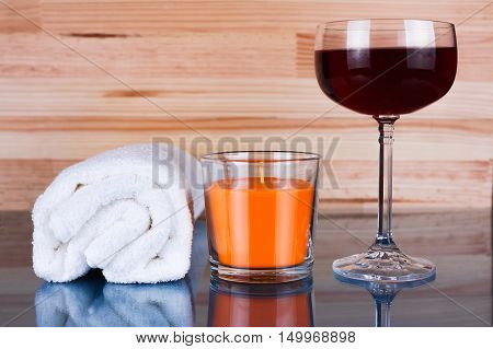 White towel orange candle and a glass of wine on natural light wooden background with reflection. Concept of sauna or spa.
