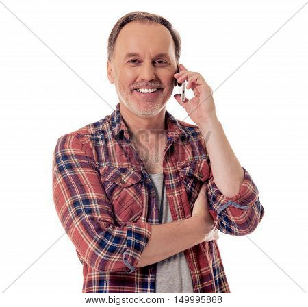 Handsome mature man in casual clothes is talking on the mobile phone looking at camera and smiling isolated on white