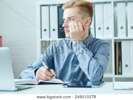 Handsome Pensive Young Business Man Sitting At The Dask With Laptop And Looking At The Window.