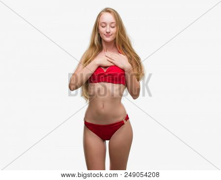 Blonde teenager woman wearing red bikini smiling with hands on chest with closed eyes and grateful gesture on face. Health concept.