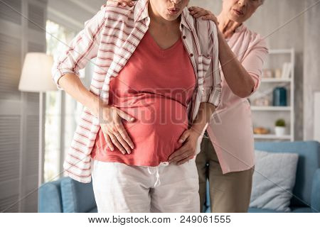 Unexpected Pain. Pregnant Woman Wearing White Baggy Trousers And Striped Shirt Feeling Unexpected Pa