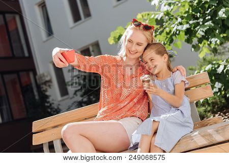 Our Photo. Pleasant Nice Woman Taking A Selfie While Sitting Together With Her Daughter On The Bench