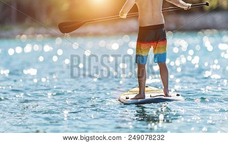 Detail of young man standing on paddleboard. Paddleboarding is the modern way of transportation and water activity sport.