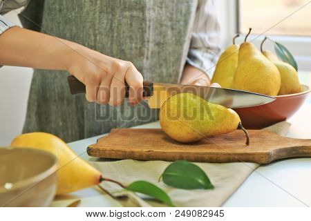 Young woman cutting fresh ripe pear on wooden board