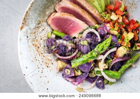 Modern fried tuna fish sashimi filet salad with green asparagus blue potatoes und vegetable chili relish as top view on a plate with copy space 