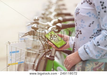 Woman using smartphone to rent bicycle from urban bicycle sharing station