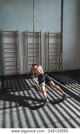 Young Fit Man In Gym Working Out With Climbing Rope. Rear View.