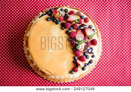 A Birthday Cake On A Glass Stand On The Table, Fruit On Top. Red Background. Top View.