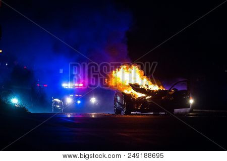 Car On Fire At Night With Police Lights In Background