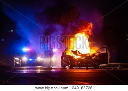 Car On Fire At Night With Police Lights In Background