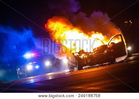 Car On Fire At Night With Police Lights In Background