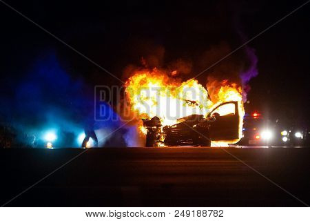 Car On Fire At Night With Police Lights In Background