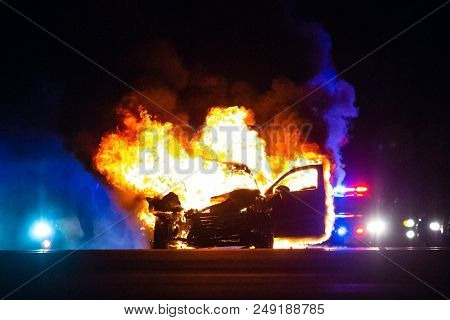 Car On Fire At Night With Police Lights In Background