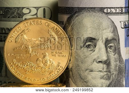 Pure Gold Eagle Coin In Front Of Benjamin Franklin Face On Rolled Bankrolls Of Usa Dollar Bills