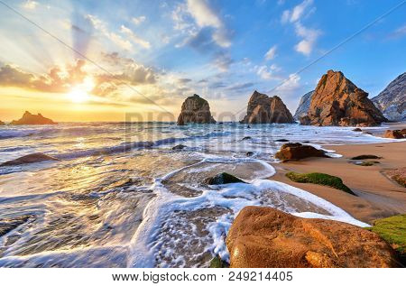 Portugal Ursa Beach at atlantic coast of Atlantic Ocean with rocks and sunset sun waves and foam at sand of coastline picturesque landscape panorama. Stones with green moss.