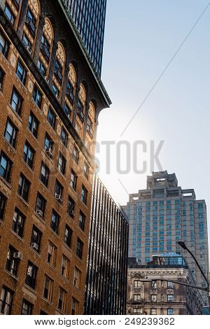 Low Angle View Of Modern And Old Buildings Against Sky In Midtown Of Manhattan With Sun Flare