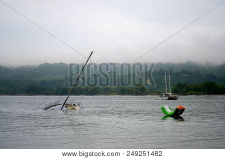 A Large Floating Water Toy Is Near A Half-sunken Yacht. A Catamaran Is In The Distance. The Sky Is O