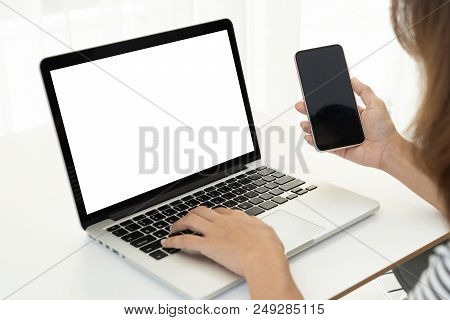 Back View. Young Business Woman Sitting In Office At Table And Using Smartphone. On Desk Is Laptop A