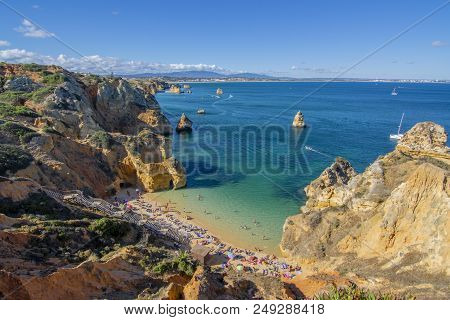 Crowd Of People Sunbathing And Enjoying Under Colorful Umbrellas In Popular Praia Do Camilo Near Pon