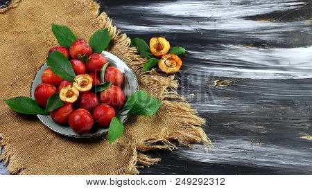 Plums. Red Sweet Plums With Green Leaves On A Round Plate And Old Cloth On A Dark Background. Flat L