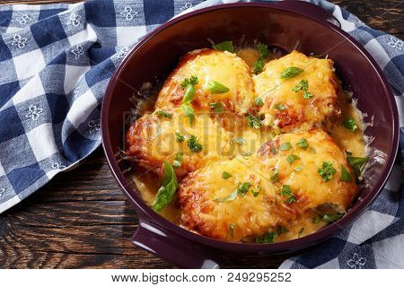 Cheesy Smothered Pork Chops Sprinkled With Basil Leaves In A Baking Dish On An Old Dark Rustic Table