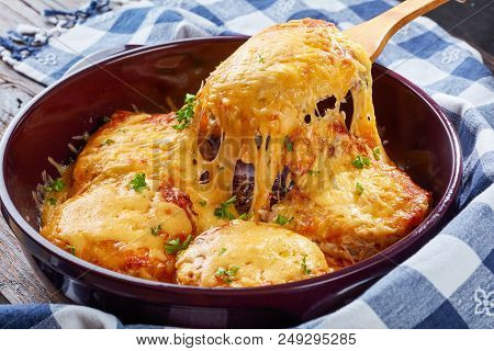 Pork Chop Topped With Onions, Mayo And 	
Stringy Melted Cheese On A Wooden Spoon In A Baking Dish On
