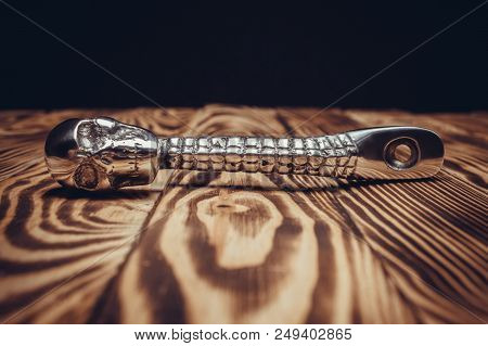 Kickstarter Pedal For A Motorcycle With A Skull On A Wooden Background