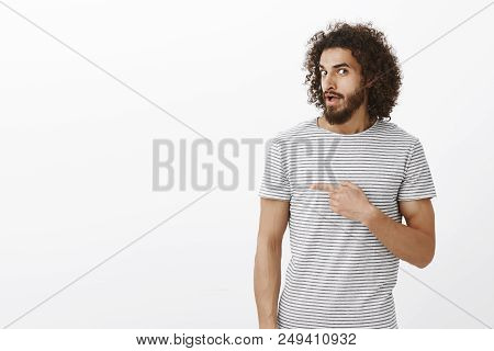 Interested Hot Hispanic Guy With Beard And Afro Hairstyle, Turning At Camera, Pointing Right While S